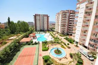 Luxuriöser Wohnkomplex mit Pool und Tennisplatz. Luftaufnahme eines modernen Wohnkomplexes mit mehreren Apartmentgebäuden, einem großen Swimmingpool, einem Tennisplatz und angelegten Gärten, die exzellente Außenanlagen zeigen.