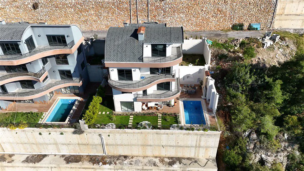 Moderne Hangvilla mit privatem Pool und Garten. Luftaufnahme einer modernen Villa am Hang mit privatem Swimmingpool, angelegtem Garten und mehreren geschwungenen Balkonen. Mit Außen-Essbereich, der zeitgenössische Architektur präsentiert.