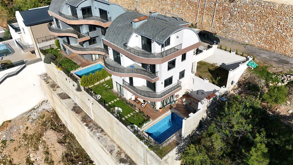 Moderner Apartmentkomplex am Hang mit Privatpools. Luftaufnahme einer zeitgenössischen Wohnanlage mit weißen Gebäuden, geschwungenen Balkonen, privaten Gärten und Swimmingpools an einem terrassierten Hang.