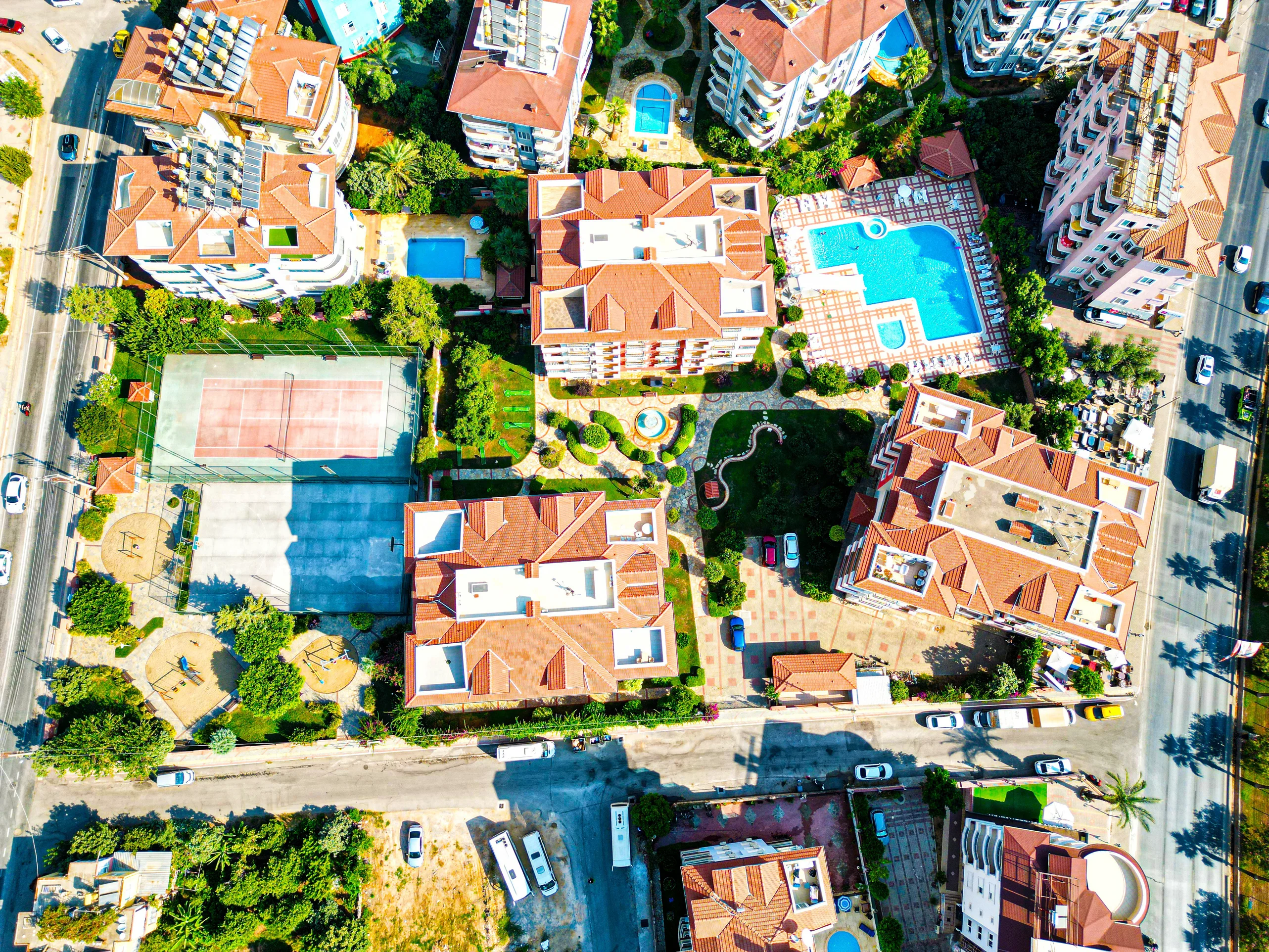 Luftaufnahme Wohnkomplex mit Pools, Tennis, Gärten. Luftaufnahme einer modernen Wohnanlage mit mehreren Gebäuden mit orangefarbenen Dächern, großen Swimmingpools, einem Tennisplatz und üppigen grünen Gärten. Inklusive eines Kinderspielplatzes.