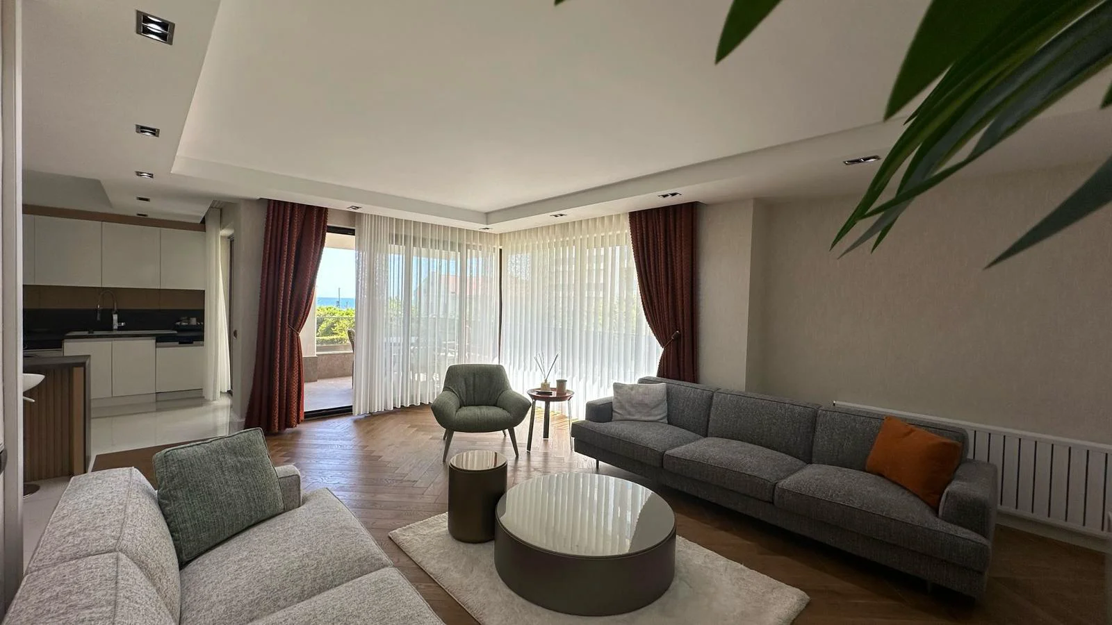 Modernes offenes Wohnzimmer mit Meerblick-Balkon. Geräumiges modernes Wohnzimmer mit Fischgrätparkettboden, großen Fenstern, Einbauleuchten und teilweisem Meerblick. Es umfasst eine offene Küche und Zugang zu einem Balkon.