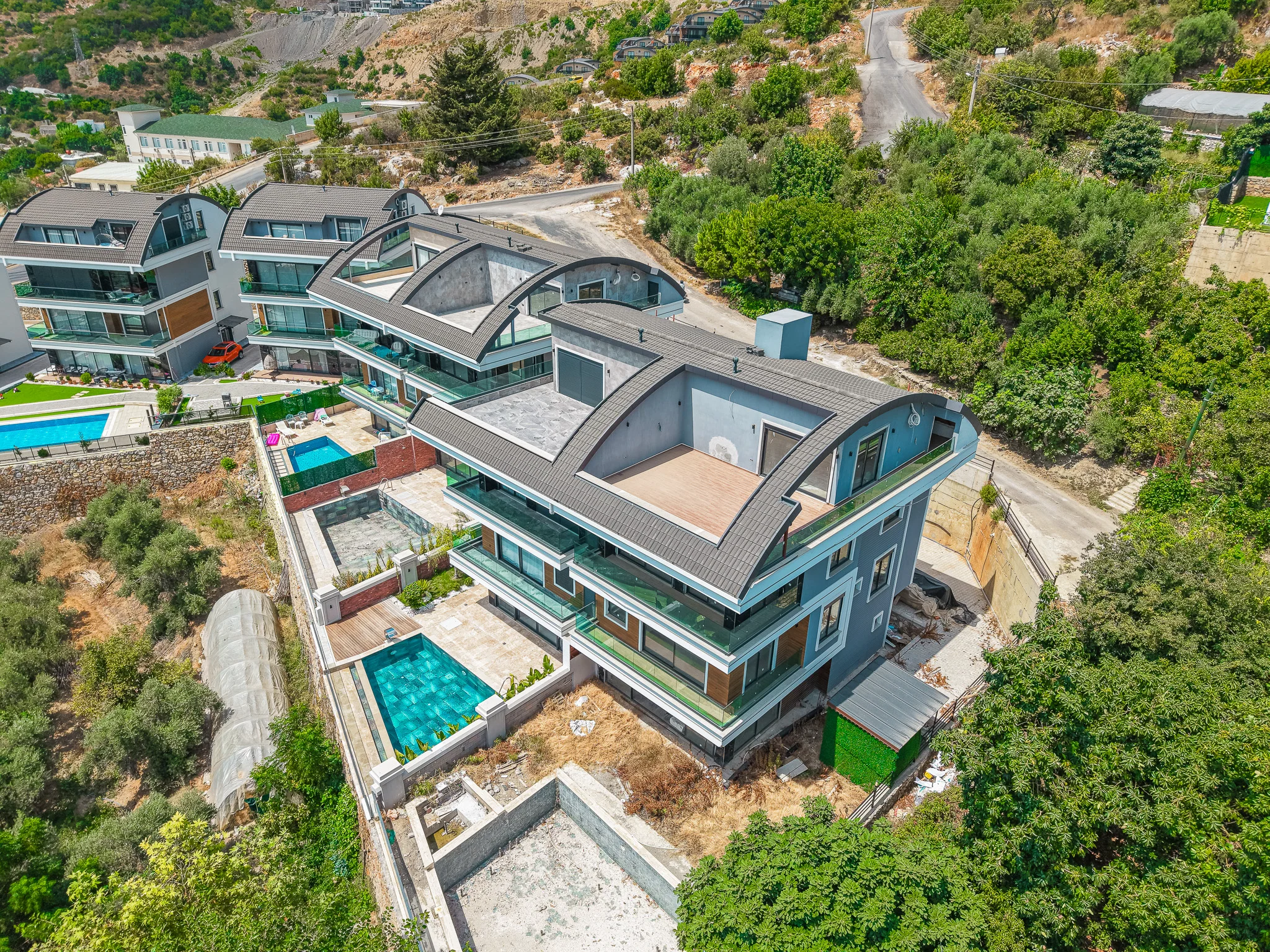 Moderne Villen am Hang mit privaten Pools und Balkonen. Luftaufnahme einer modernen Wohnanlage mit mehreren Villen und privaten Pools. Zeitgenössisches Design mit geschwungenen Dächern, gelegen an einem grünen Hang in der Türkei.