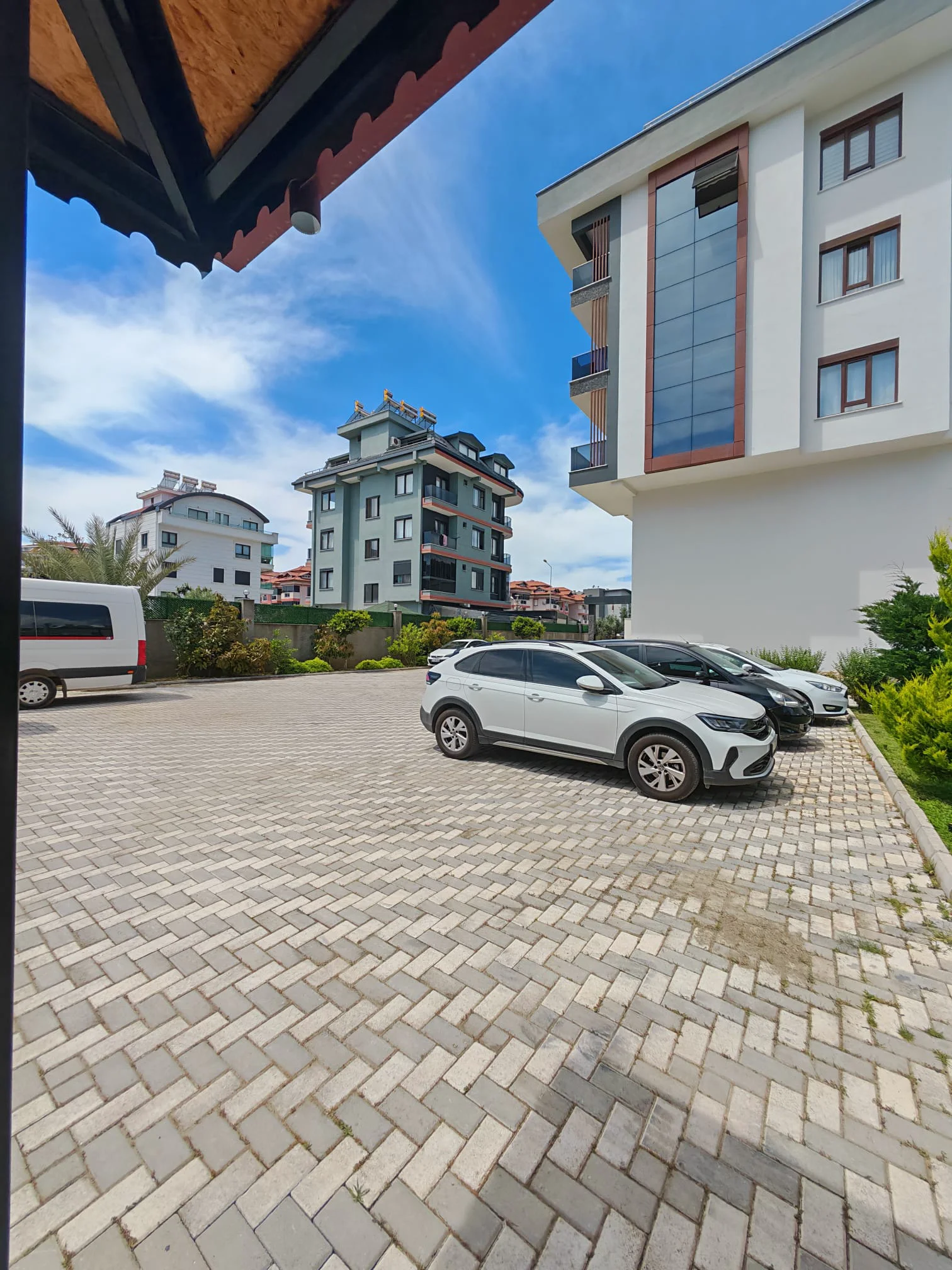 Geräumiger Außenparkplatz mit gepflasterter Fläche. Außenparkplatz mit hell- und dunkelgrauen Verbundpflastersteinen, der viel Platz für mehrere Fahrzeuge vor modernen Apartmentgebäuden unter klarem blauem Himmel bietet.