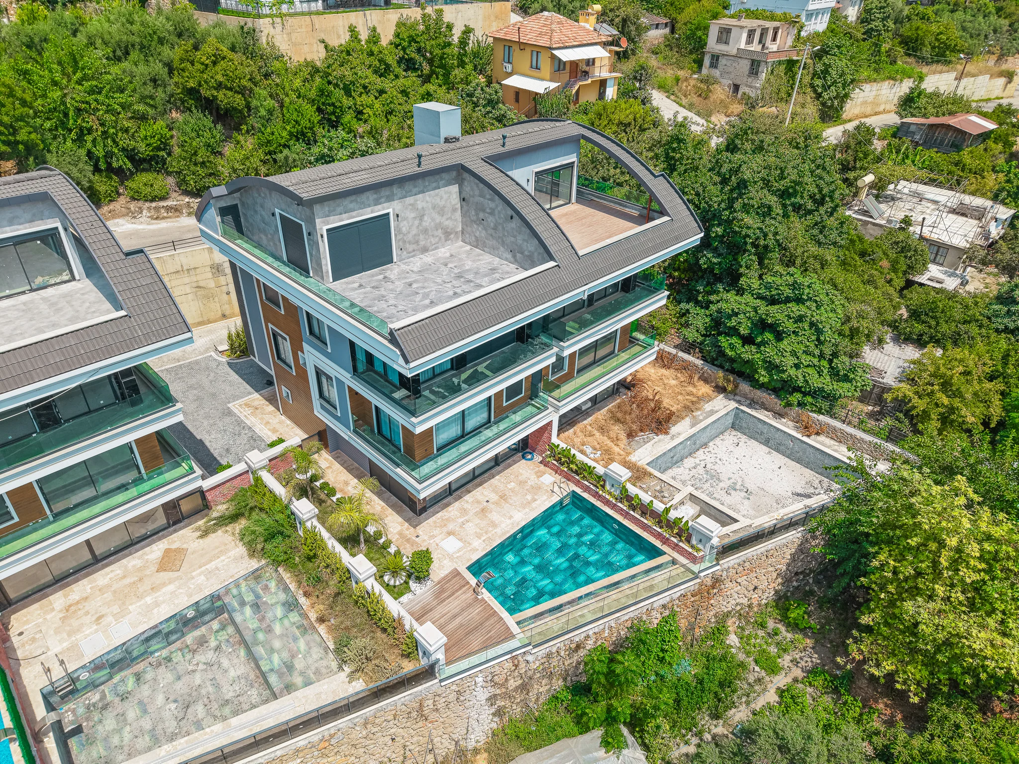 Modernes Apartmentgebäude mit privatem Pool und Balkonen. Luftaufnahme eines modernen mehrstöckigen Apartmentgebäudes mit elegantem Design, Glasbalkonen und einem privaten Außenpool. Das zeitgenössische Bauwerk ist von üppigem Grün umgeben.