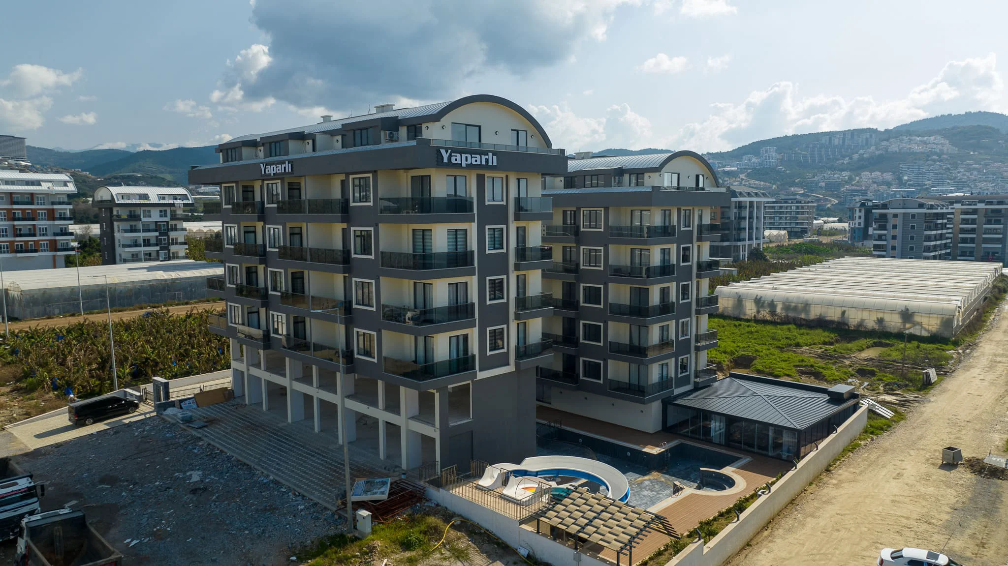 Moderne Apartmentanlage mit Pool und Bergblick. Moderne Wohnanlage „Yaparlı“ mit zwei mehrstöckigen Gebäuden, privaten Balkonen und einem Außenpoolbereich. Zur Ausstattung gehören ein Sozialgebäude und ein Panoramablick auf die Berge.