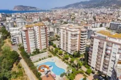Modernes Apartmentkomplex mit Pool und Panoramameerblick. Luftaufnahme eines modernen Wohnkomplexes mit Hochhaus-Apartmentgebäuden und einem großen Schwimmbad mit Wasserrutsche. Stadt, Meer und Berge sind sichtbar.