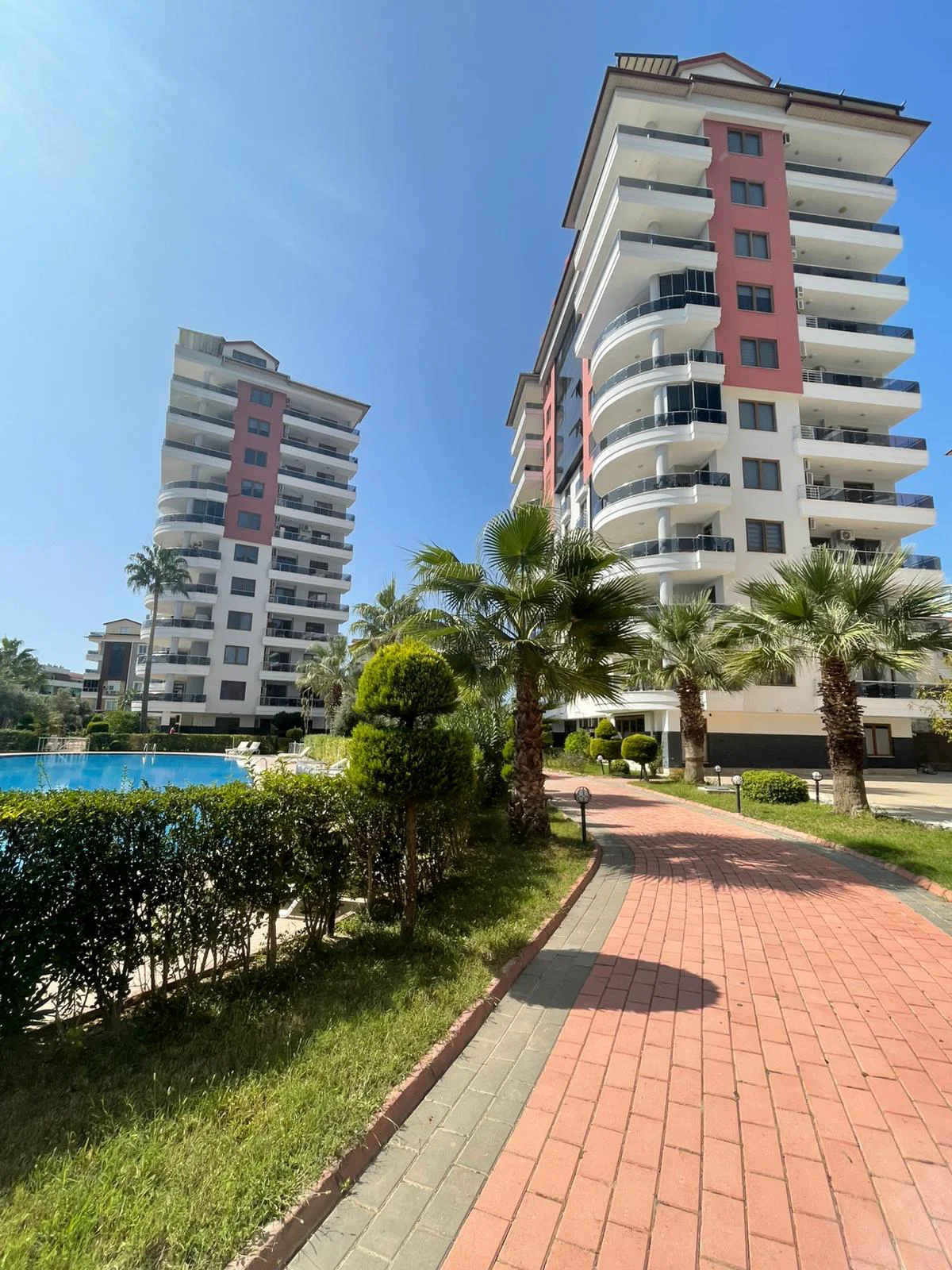 Moderne Apartmentgebäude mit Pool und angelegtem Garten. Außenansicht einer modernen Wohnanlage in der Türkei mit zwei Hochhäusern, einem großen Swimmingpool und tropischen Palmen in einem gepflegten Garten.