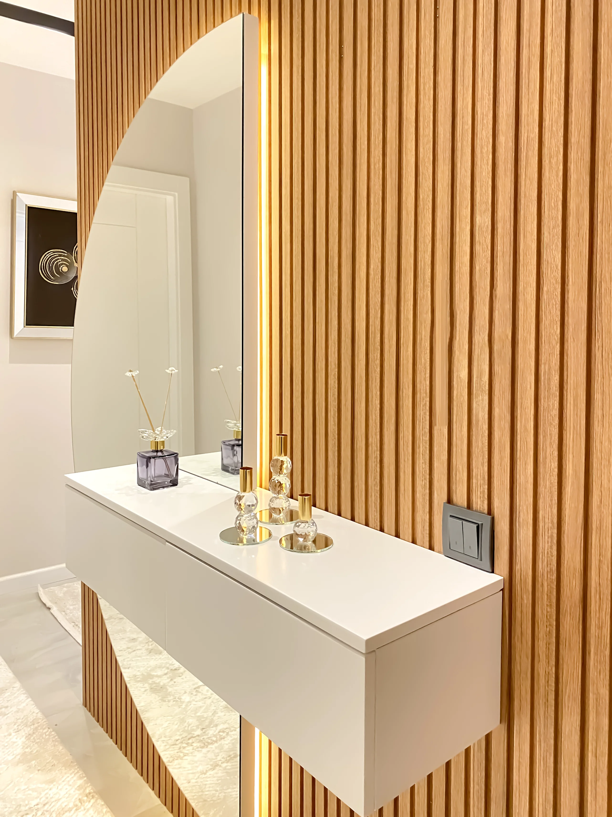 Stilvoller Moderner Eingangsbereich mit Holzlamellenwand und Bogenspiegel. Ein moderner Eingangsbereich mit einer stilvollen Holzlamellenwand, einem großen Bogenspiegel mit integrierter LED-Beleuchtung und einem weißen schwebenden Konsolentisch. Dekoriert mit eleganten Accessoires. Renoviertes und zeitgemäßes Design.