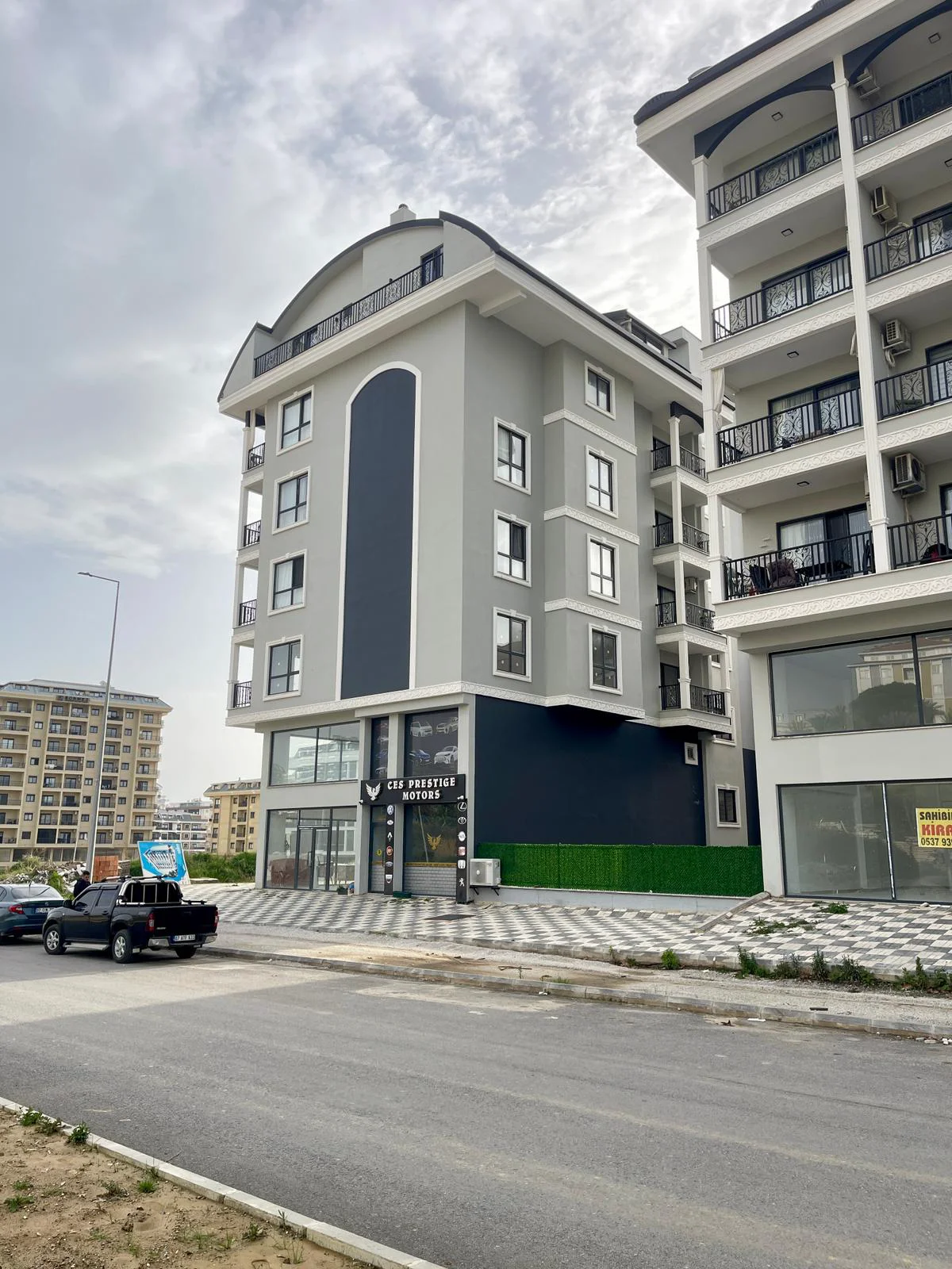 Moderne Außenansicht eines Wohn- und Geschäftshauses mit Ladenlokalen im Erdgeschoss. Außenansicht eines modernen, neu errichteten Wohn- und Geschäftshauses mit einer grau-dunkelgrauen Fassade, bogenförmigen architektonischen Details und einer Gewerbeeinheit im Erdgeschoss.