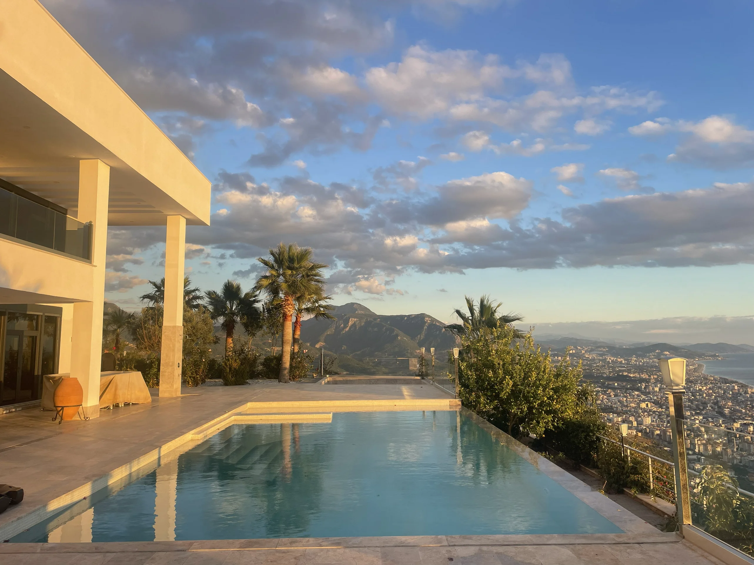 Luxusvilla mit Infinity-Pool und Panoramameerblick. Außenansicht einer modernen Luxusvilla mit einem glitzernden Infinity-Pool mit Treppenstufen. Sie bietet einen atemberaubenden Panoramablick auf die Stadt, die Berge und das Mittelmeer.