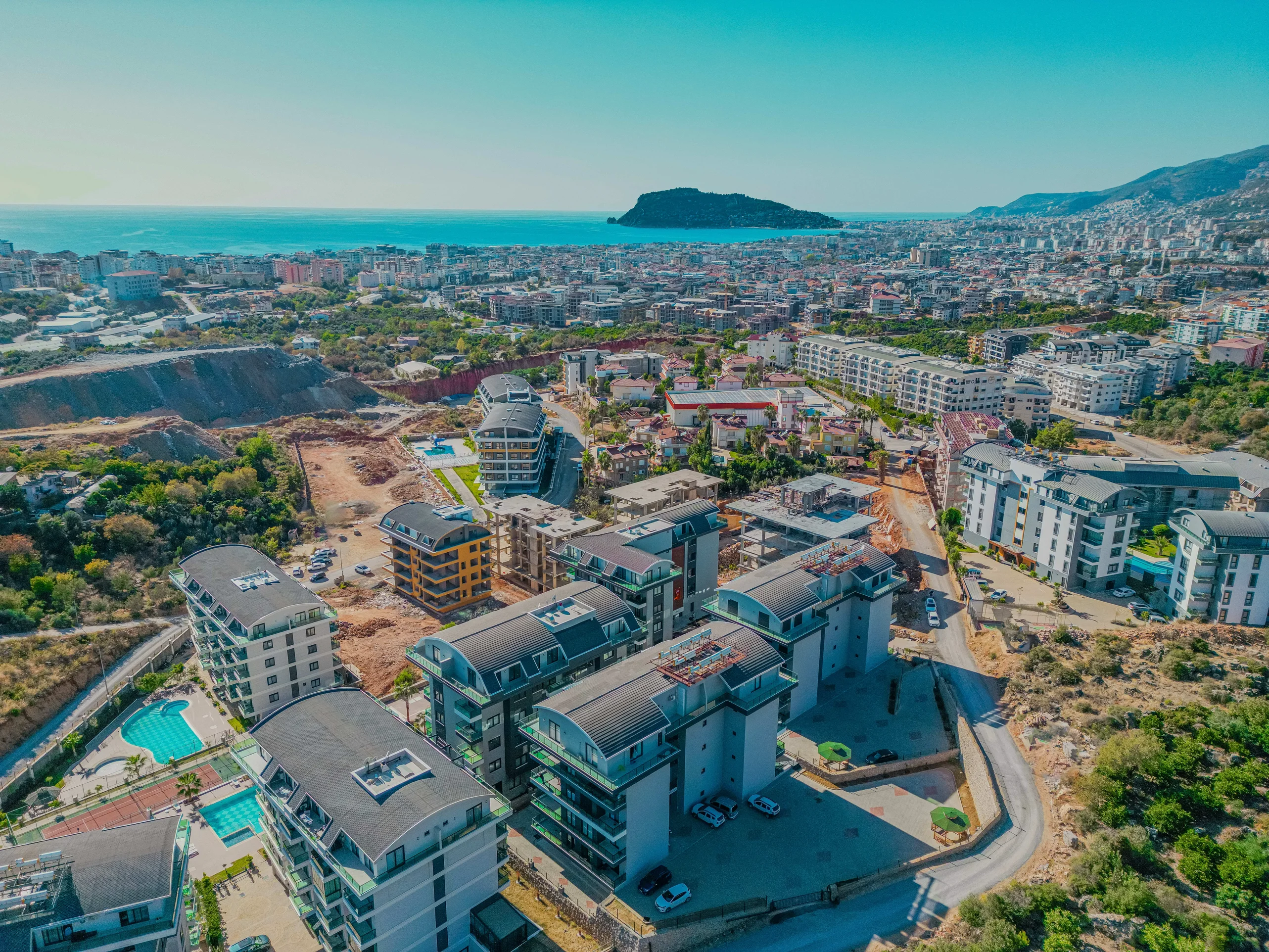 Alanya Skyline: Neue Residenzen und Blick auf das Mittelmeer. Luftaufnahme moderner Wohngebäude mit Swimmingpools in der lebhaften türkischen Küstenstadt Alanya, mit atemberaubendem Blick auf das Mittelmeer und die Insel.