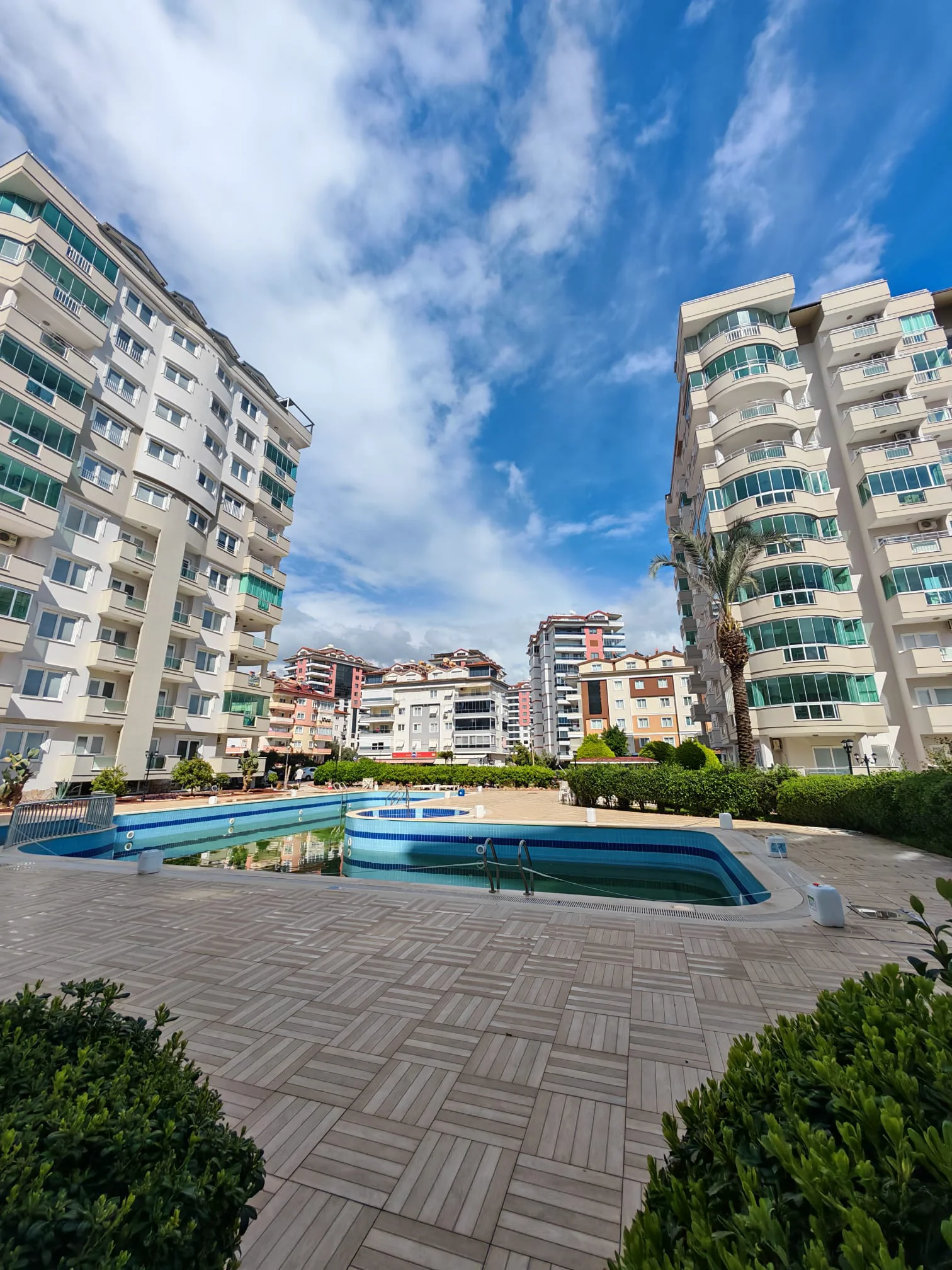 Wohnanlage mit Außenpool. Außenansicht einer modernen Wohnanlage mit zwei hohen Apartmentgebäuden, einem Außenpool und gepflegten Gartenanlagen unter klarem Himmel.