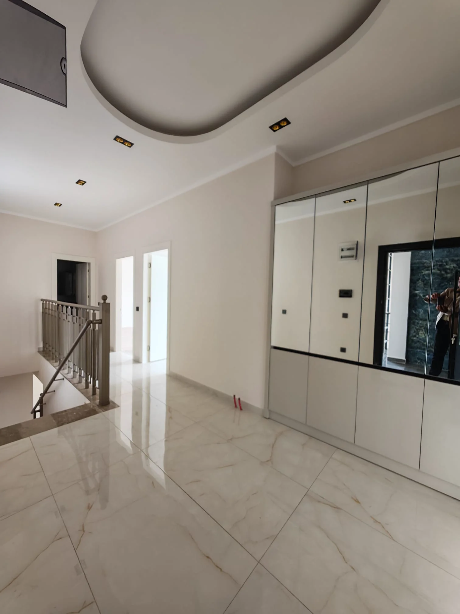 Moderner Flur mit Spiegelschrank und Einbaustrahlern. Heller Flur im Obergeschoss mit modernen Fliesen in weißer Marmoroptik und stilvoller Einbaubeleuchtung. Mit integriertem Spiegelschrank und einer eleganten Metalltreppe.