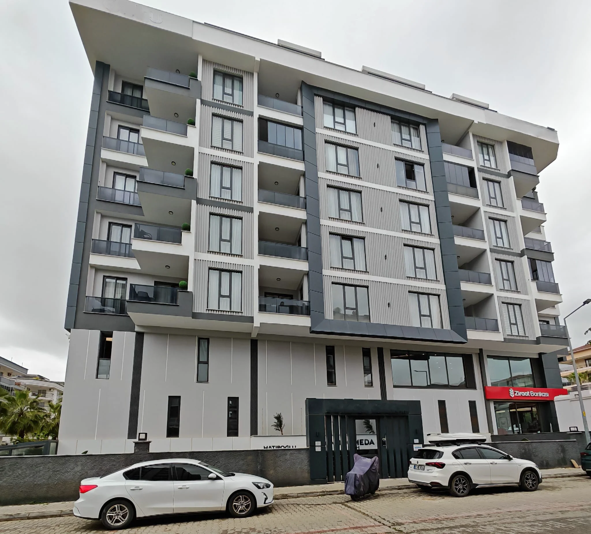 Modernes mehrstöckiges Mehrfamilienhaus Außenansicht mit Balkonen. Außenansicht eines modernen mehrstöckigen Wohngebäudes mit einer eleganten grau-weißen Fassade. Es verfügt über zahlreiche Balkone mit Glasgeländern und großen Fenstern, die zeitgenössische Architektur präsentieren.