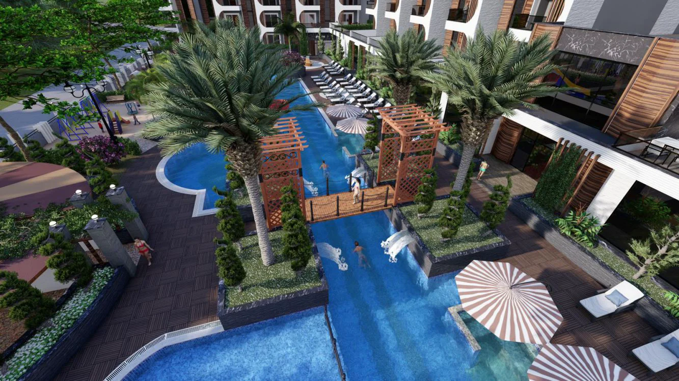 مجمع سكني فاخر يضم عدة حمامات سباحة خارجية. منظر جوي للمنطقة الخارجية لمجمع سكني حديث يضم عدة حمامات سباحة، وجسرًا رابطًا، وأشجار نخيل مورقة، وكراسي استلقاء للتشمس، وملعبًا قريبًا.
