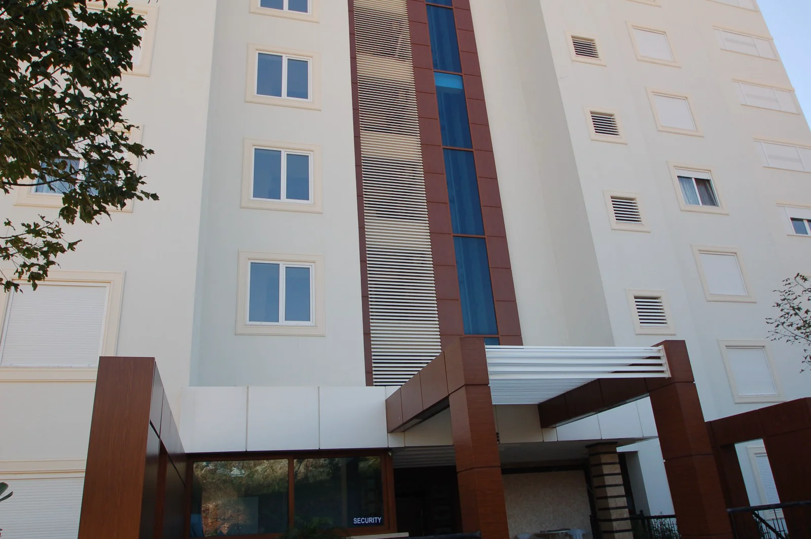 Modern Building Exterior with Brown Architectural Elements. Exterior of a modern multi-story building with a light facade and prominent brown architectural entrance. Features include multiple windows and vertical blue glass panels, highlighting a contemporary design.