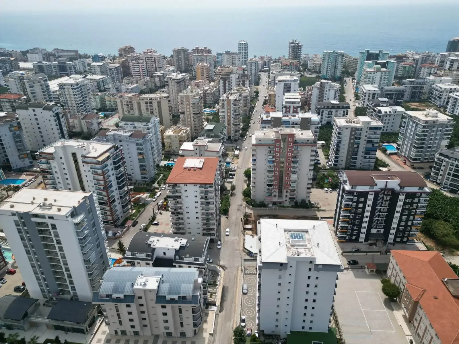 Panoramic Cityscape with Coastal Views, Modern Urban Living. An aerial view of a dense urban area featuring numerous modern apartment buildings, winding streets, and scattered green spaces, all set against the clear blue sea in the distance, portraying a vibrant city.