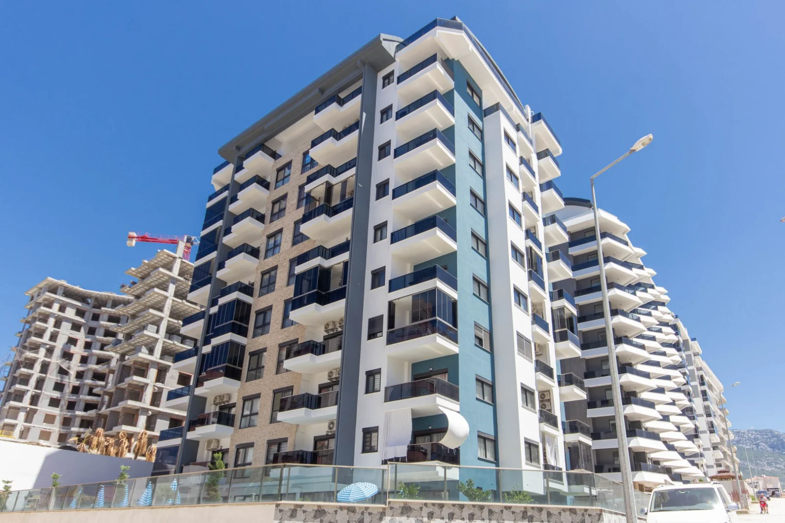 Modern Apartment Building Exterior with Multiple Balconies. Exterior view of a newly built, modern apartment building featuring a striking white, blue, and beige facade with multiple dark-glass balconies, under a clear sky.