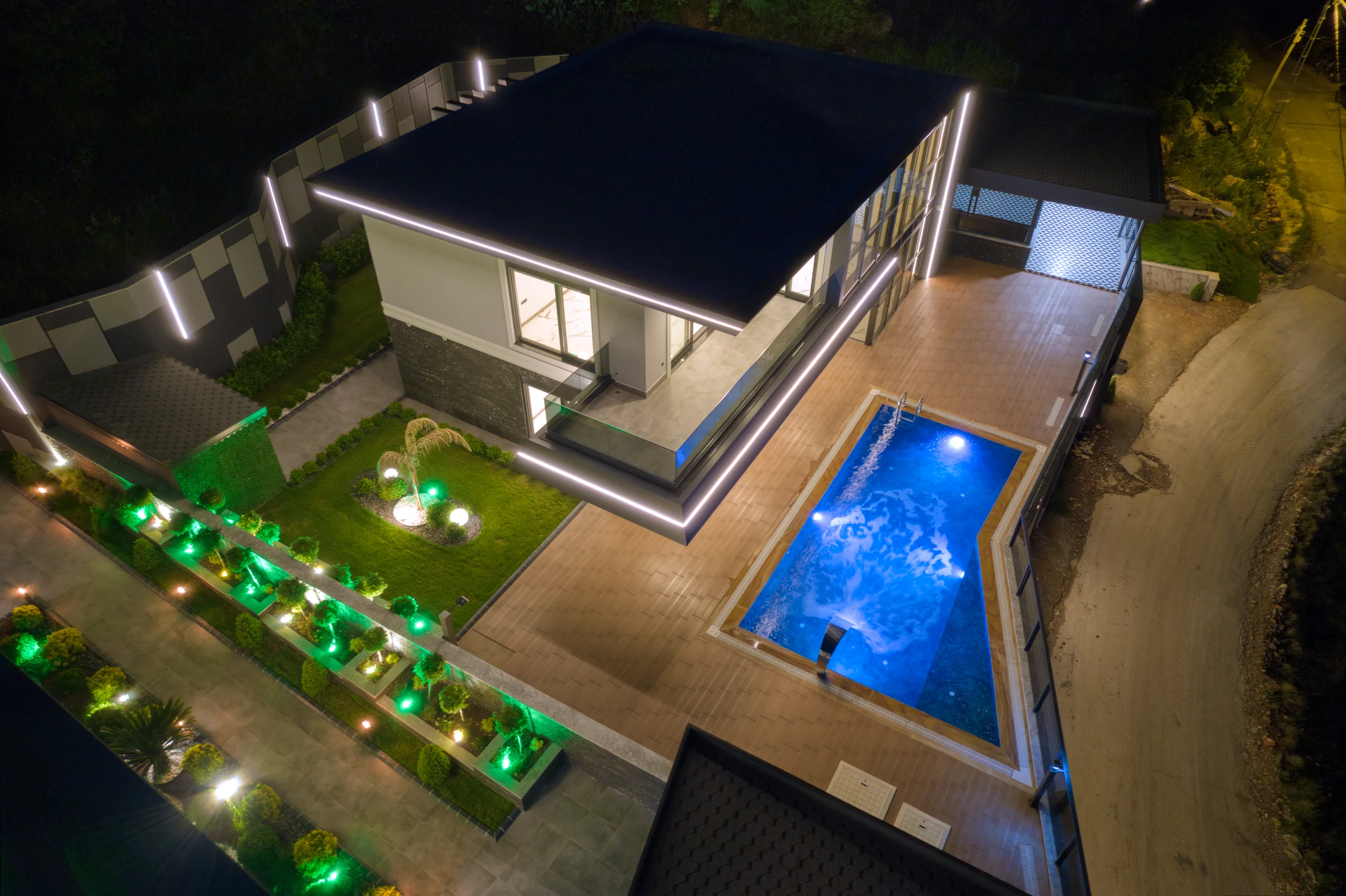 Luxurious Modern Villa with Stunning Private Pool. Aerial night view of a modern two-story villa. Features a bright blue illuminated swimming pool, a beautifully lit landscaped garden, and stylish exterior lighting, showcasing luxurious outdoor amenities.