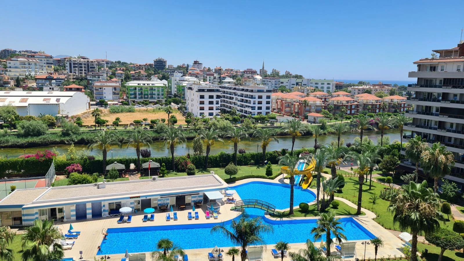 Panoramic River, Resort Pool, City, and Sea View. Panoramic view from a property, showcasing a vibrant resort pool, a winding river, an expansive cityscape, and the distant Mediterranean Sea.